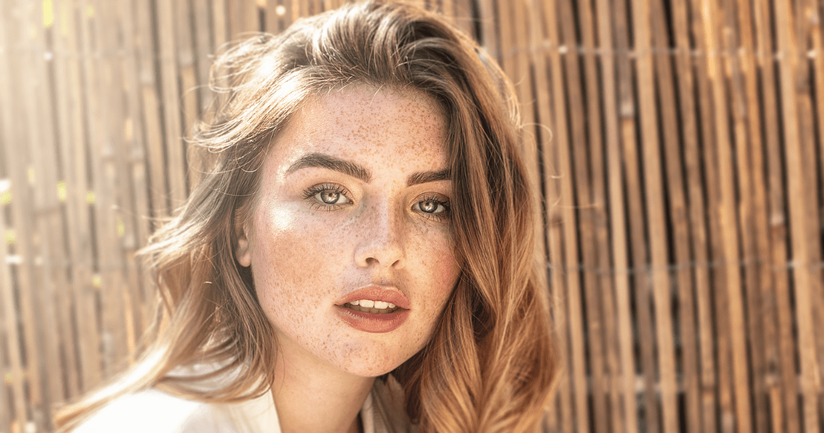 A women's portrait looking directly at the camera with freckles and a soft smile.