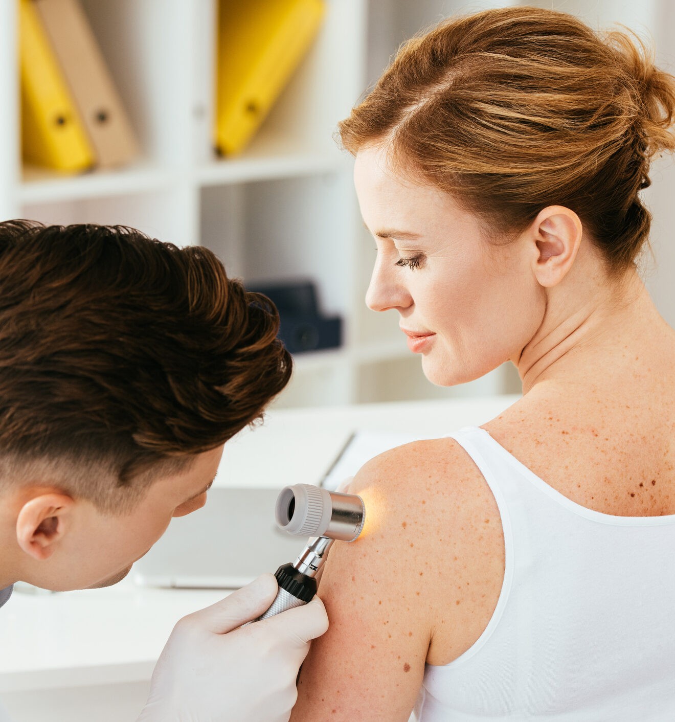 dermatologist in latex gloves holding dermatoscope while examining attractive patient with skin disease