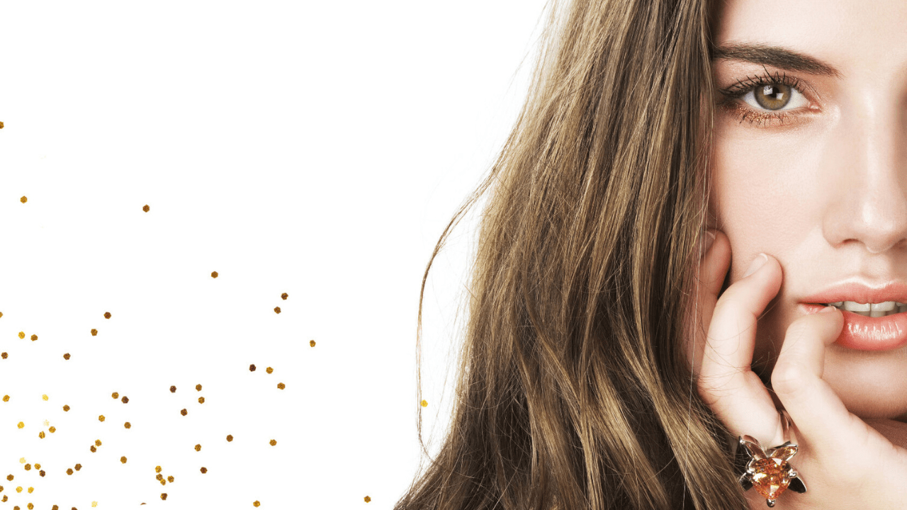 A woman with long brown hair wearing a gold ring on her finger.