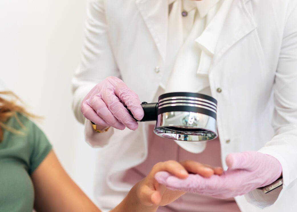 The dermatologist examines the moles or acne of the patient with a dermatoscope. Prevention of melanoma