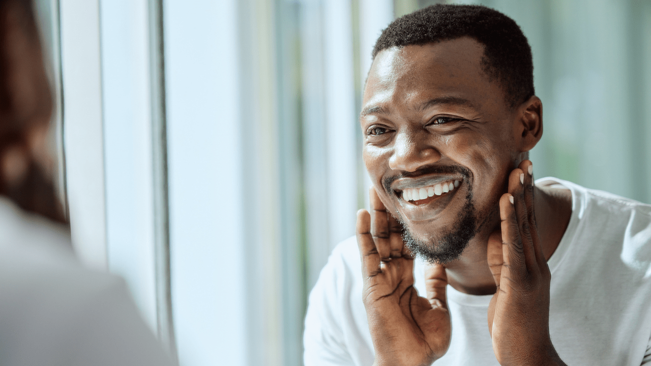 An African American man looking into the mirror and smiling.