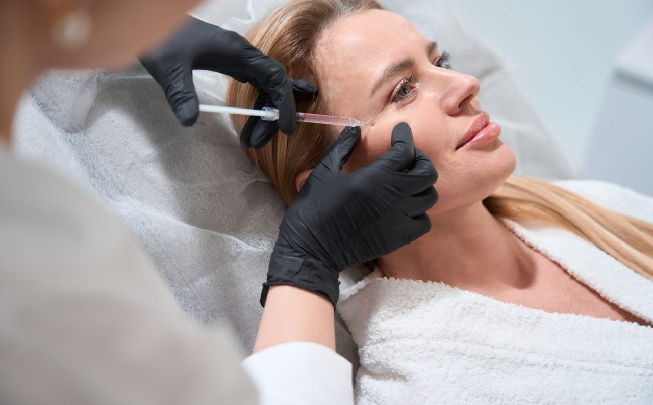 Female blonde gets a rejuvenating injection in her cheeks, an esthetician uses a thin needle